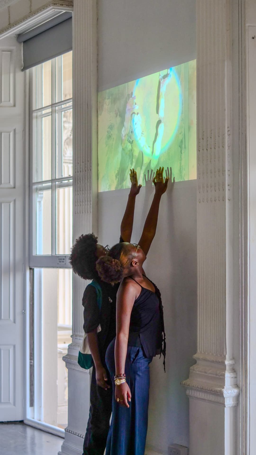 Two visitors reaching towards a projected film on the gallery wall